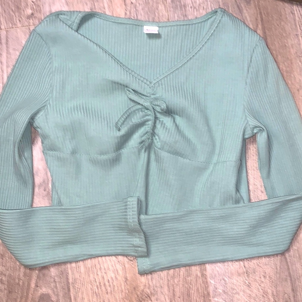 A light green top with a ribbon tied in the middle. Long sleeve top.
